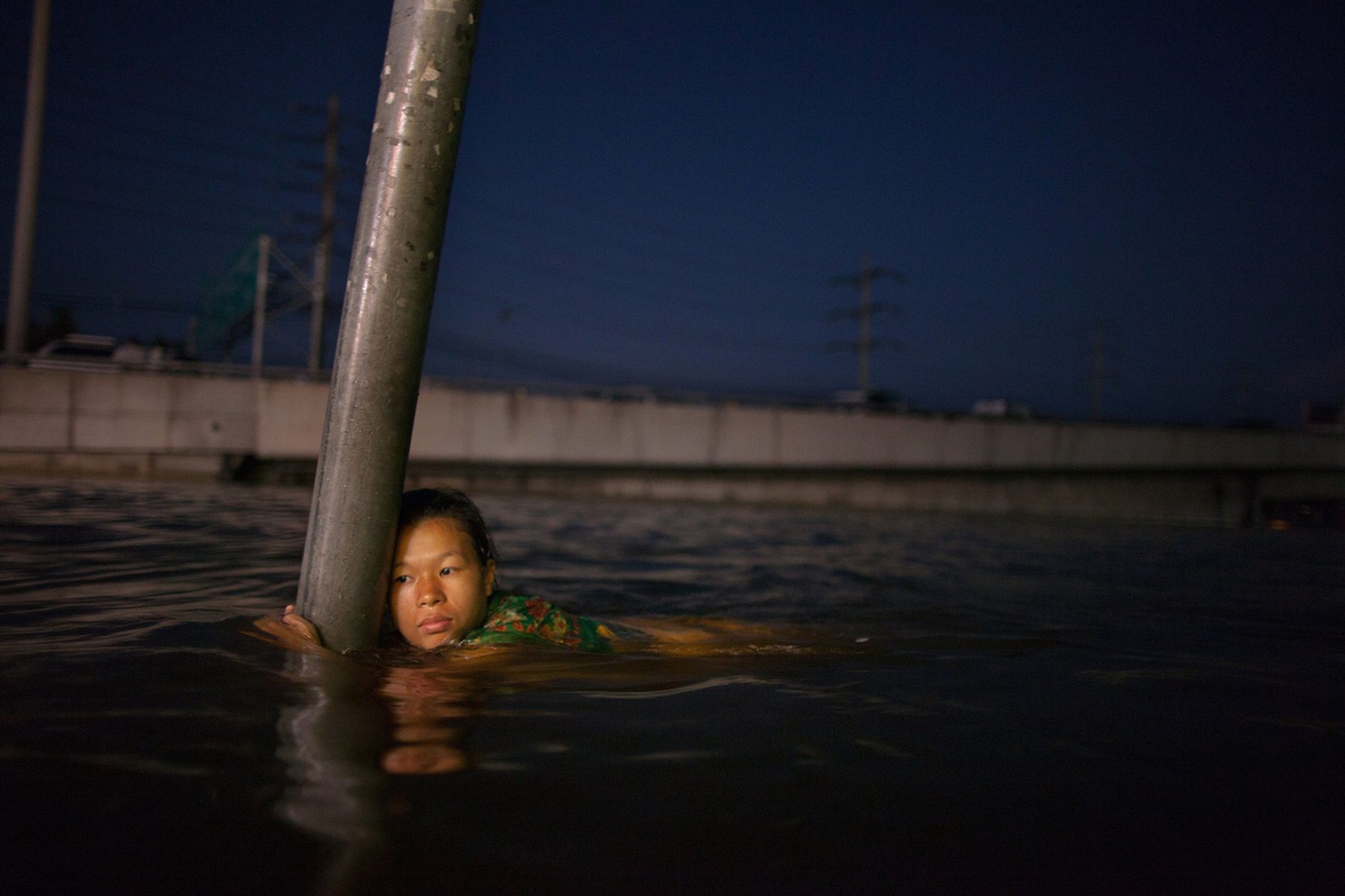 RANGSIT,THAILAND - OCTOBER 24rd: A woman hangs onto a street sign in chest deep water along the flooded streets in Rangsit on the outskirts of Bangkok October 24, 2011 in Bangkok, Thailand. Hundreds of factories closed in the central Thai province of Ayutthaya and Nonthaburi as the waters come closer to threaten Bangkok as well. Around 350 people have died in flood-related incidents since late July according to the Department of Disaster Prevention and Mitigation. Thailand is experiencing the worst flooding in 50 years with damages running as high as $6 billion which could increase of the floods swamp Bangkok.(Photo by Paula Bronstein /Getty Images)