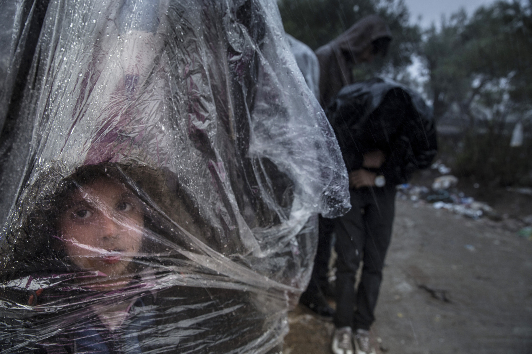 LESBOS, GREECE - OCTOBER 23:  Rain and cold weather create more suffering for refugees as Afghans stand for hours trapped at the gates waiting for their turn to register at Moria camp. Colder weather and rough seas continue to cause deaths at sea as thousands travel in overcrowded small rafts. According to the IOM, an estimated 100,000 people landed in Greece, an average of almost 4,500 per day in late October and November. Nearly all of those entering Greece on a boat from Turkey are from the war zones of Syria, Iraq and Afghanistan. (Photo by Paula Bronstein)