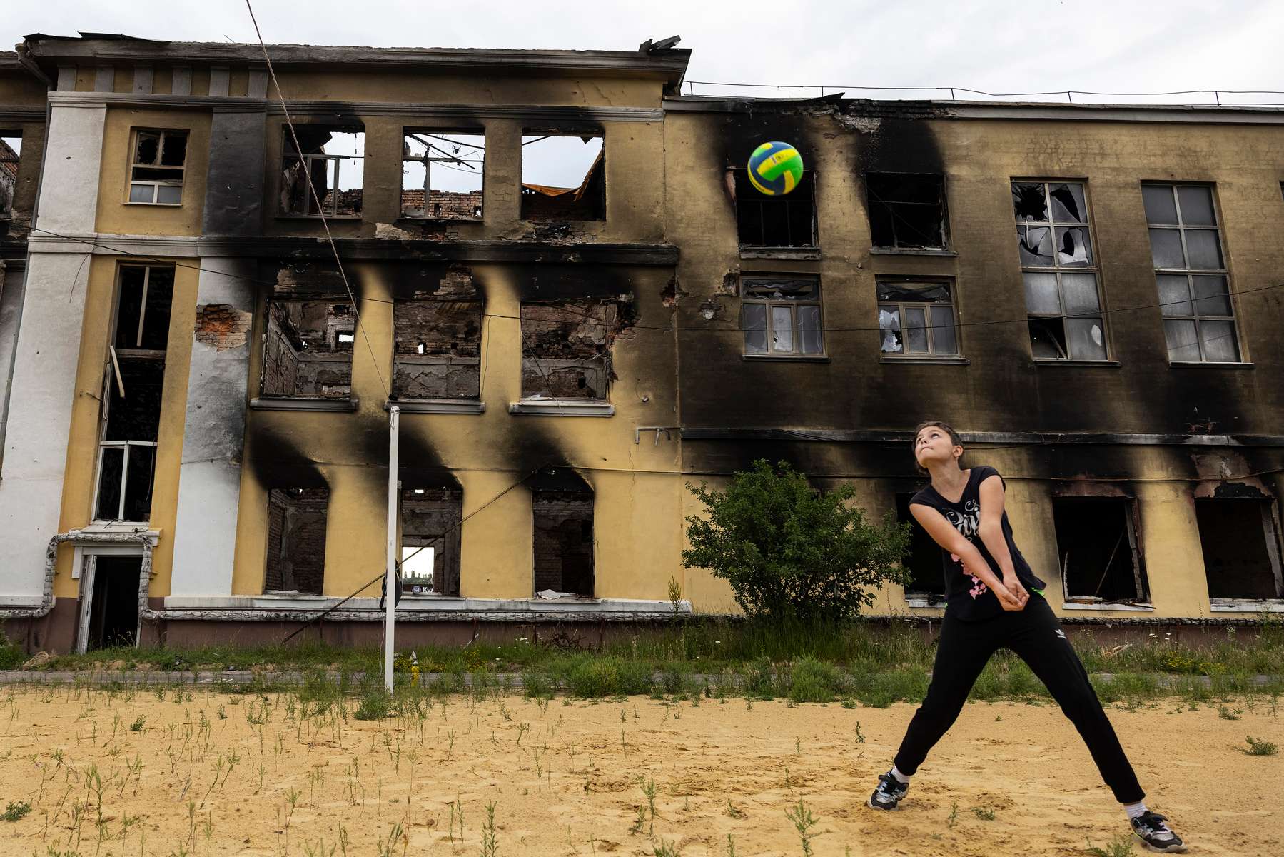 A girl plays volleyball with her father on June 24,2002  against the ruins of a school that was destroyed amongst many other educational institutions as Russian shelling hits Kharkiv constantly. 