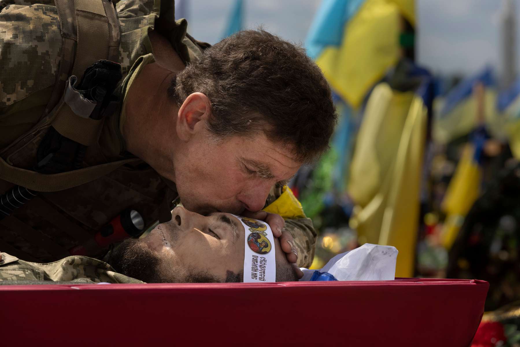 At a Kharkiv cemetery, a Ukranian soldier says goodbye with a kiss on the forehead of Maxim Shcherbak, 29,  who was killed on June 19th in the Donbas region.