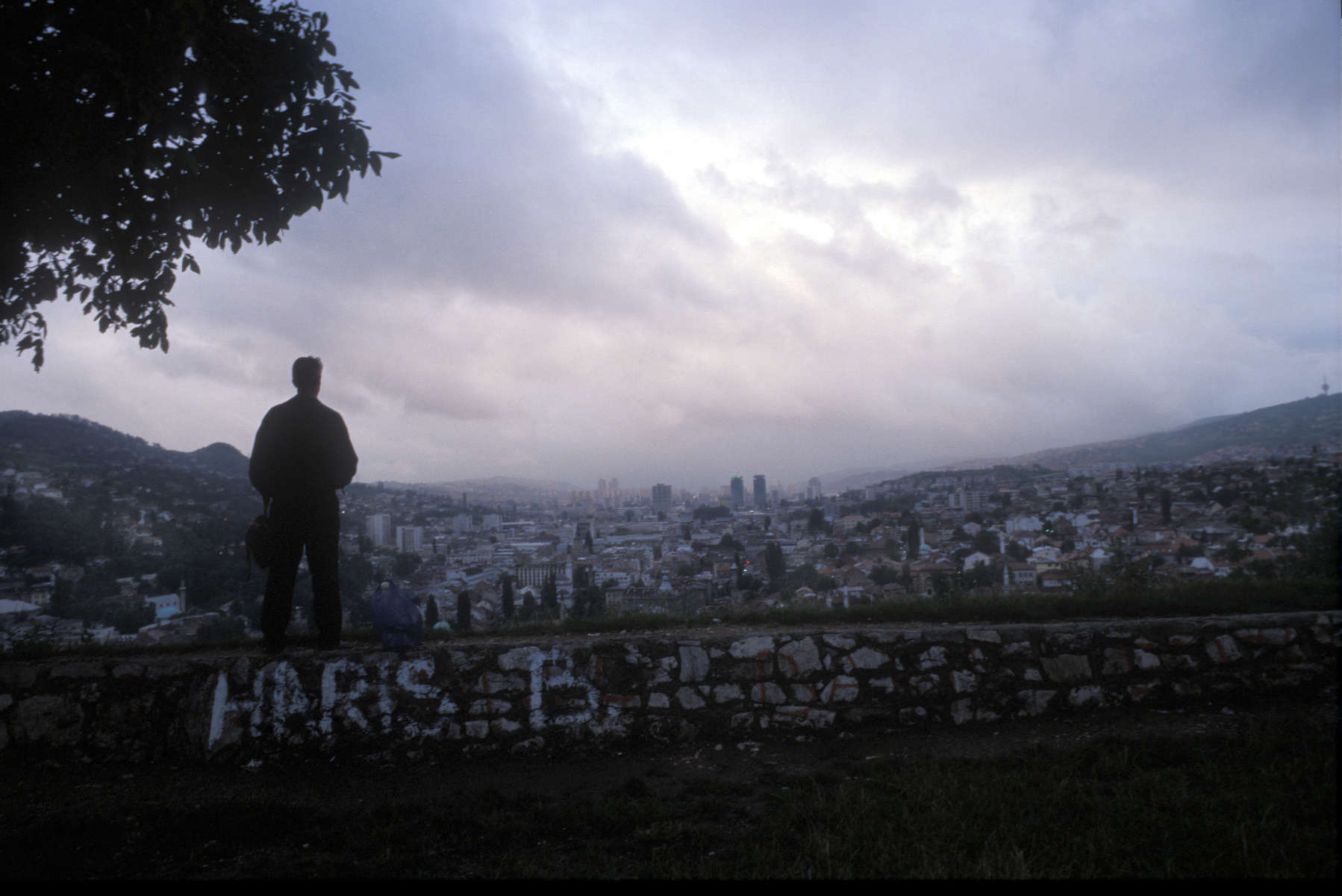 From one of the hillsides that climb up from Sarajevo, a man looks out over the city at sunset. July 2004.