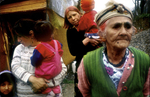 A Roma woman with her daughters-in-law and grandchildren stands in front of a makeshift home in the village of Strazenica. During the war, gypsies were also \{quote}cleansed\{quote} by Serbs; these gypsies were forced to leave their homes and have returned to rebuild.