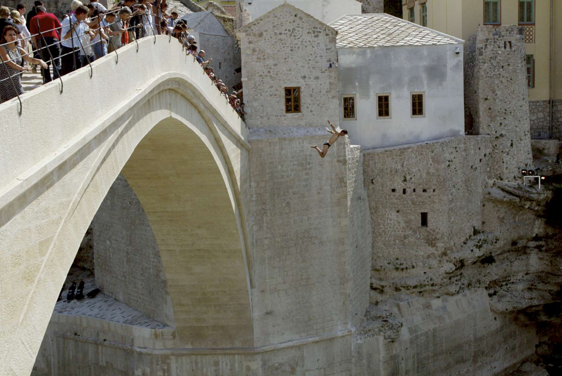 One of Mostar\'s legendary jumpers throws himself from the town\'s famed brdige, which stands more than eighty feet high. Eleven years after the bridge was destroyed during the 1992-95 war, the rebuilt structure was opened to the public after a ceremony that drew many foreign officials, including Prince Charles. Local jumpers and divers wasted no time returning to one of their favorite pasttimes before the war -- collecting change from tourists who watch them jump. Local athletes also used the week to prepare for the 448th annual jumping and diving competition, held the following week. 