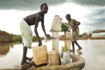 Children fetch water from the hand pump near their flooded homes.  Aweil is in a relatively low-lying location and suffers from seasonal flooding.  The floods have been exacerbated by human factors with insufficient drainage and newly constructed roads interrupting natural drainage patterns.Aweil, Northern Bahr el Ghazal State