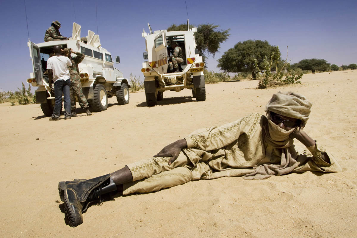 A rebel from the Sudan Liberation Army lounges in front of two  United Nations African Union Mission in Darfur (UNAMID) armoured personnel carriers during a meeting between SLA commanders and peace envoys from the UN and African Union.Umm Rai, Northern Darfur State