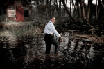 a man stands in a lake in a dark forest turned looking back 