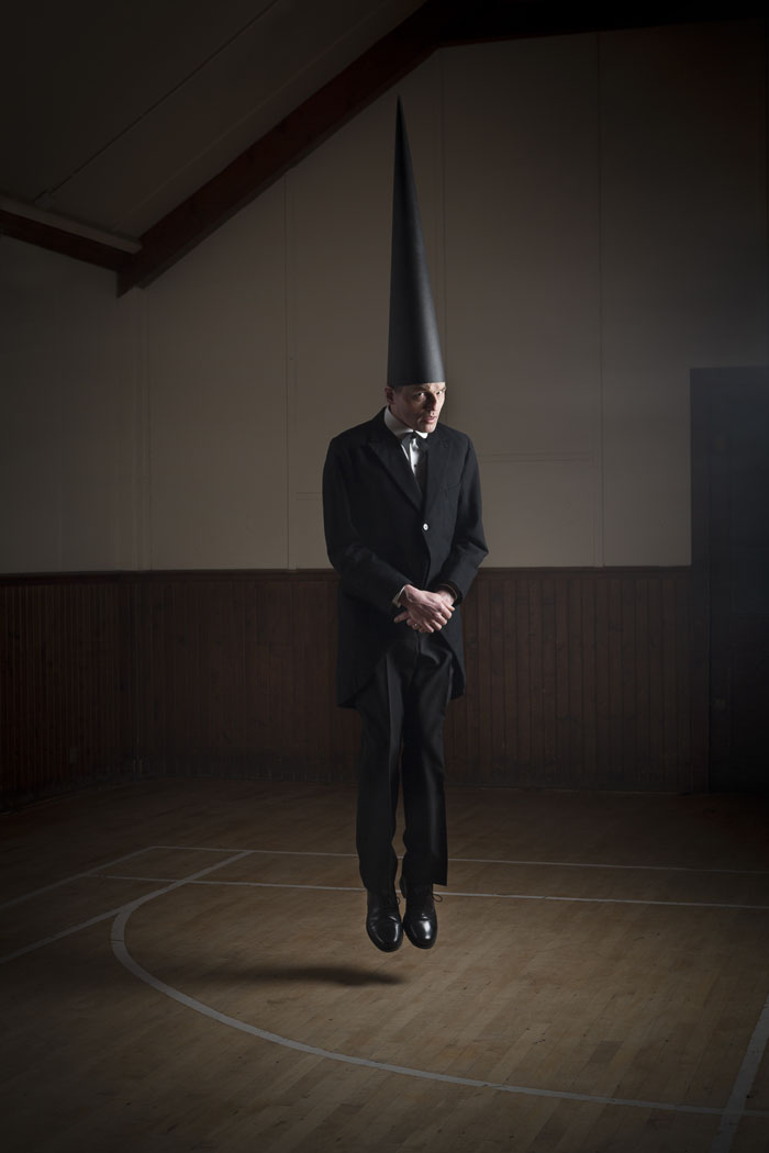 A conemen floats in a dark hall staring at the viewer. He wears black tails and a pointed black hat