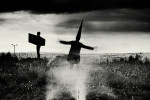 a Coneman stands before the Angel of the North flapping his arms . Black and white landscape photograph with a moody sky.