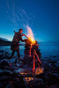 a man performas a ritual at a burning fire cairn on the edge of the sea.