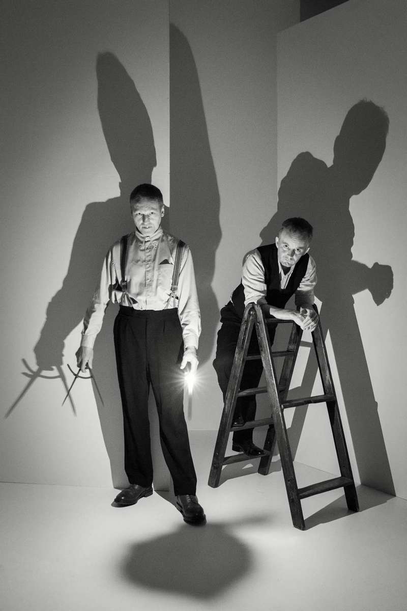 two men in a studio with calipers and a ladder lit by a single candle