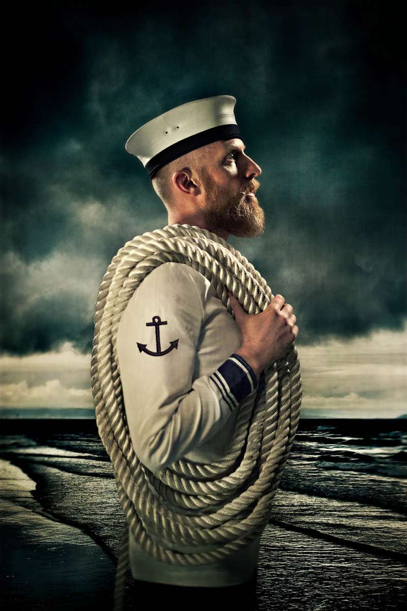 portrait of a bearded sailor at the edge of sea with a large rope over his shoulder