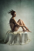 naked girl sitting on a box with fabric. Wearing feathers in her hair. Painterly colour nude of a beautiful woman
