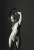 standing nude girl in a studio stretching her arms. Dark fine art beautiful girl