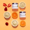 InstaNatural's Brightening Vitamin C Scrub photographed on orange with the natural ingredients of strawberry and citrus.