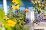 A polished pewter cup is photographed on a railing with flowers for the Danforth Pewter catalog.