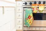 Floral patterned oven mits and a tea towel hang off an oven door in this catalog photo for April Cornell.