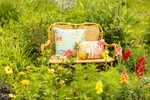 A bench sits in a green, flowering field with color pillos. Photographed for the April Cornell catalog.