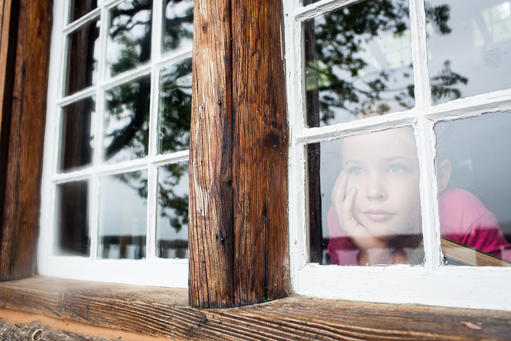 Young girl looking outside through window reflection. by Vermont photographers at Reciprocity Studio, Burlington