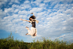 Young woman jumps for joy in front of clouds and blue sky on a summer day.