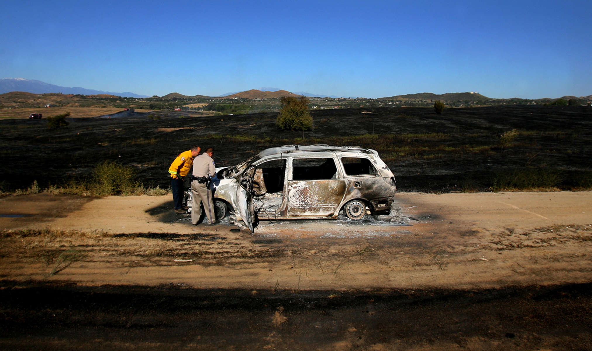 Lake Matthews station Battalion Chief Greg Everhart, left, and California Highway Patrol officer Tony Coronado examine a burnt vehicle on a dirt road near Gavilan Road in Riverside, Calif. According to Cal Fire, a motorist was driving the vehicle whenit caught fire and then burned 45 acres of brush.  (The Press-Enterprise/ Mark Zaleski)