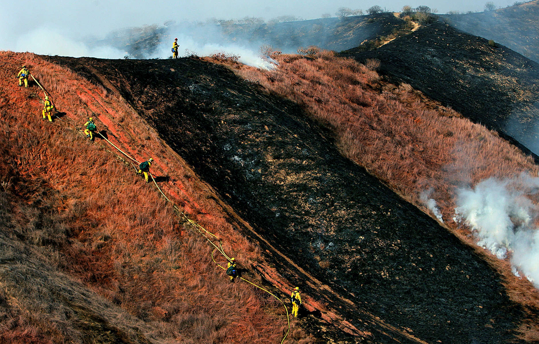 Firefighters carry a hose line to extinguish spot fires after fire retardant was dropped in a canyonnear homes on Parvin Lane in Colton, Calif. No homes were damaged in the 20-acre brush fire. (The Press-Enterprise/ Mark Zaleski)