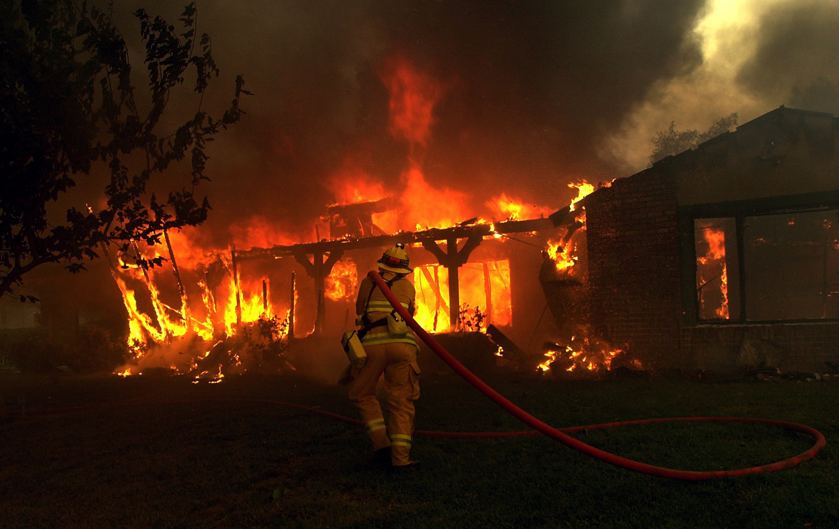 San Manuel firefighter Laurie Green movesin to extinguish a house engulfed in flamesin San Bernardino, Calif. Hundreds of homes were destroyed in the Old Fire. (The Press-Enterprise/ Mark Zaleski)