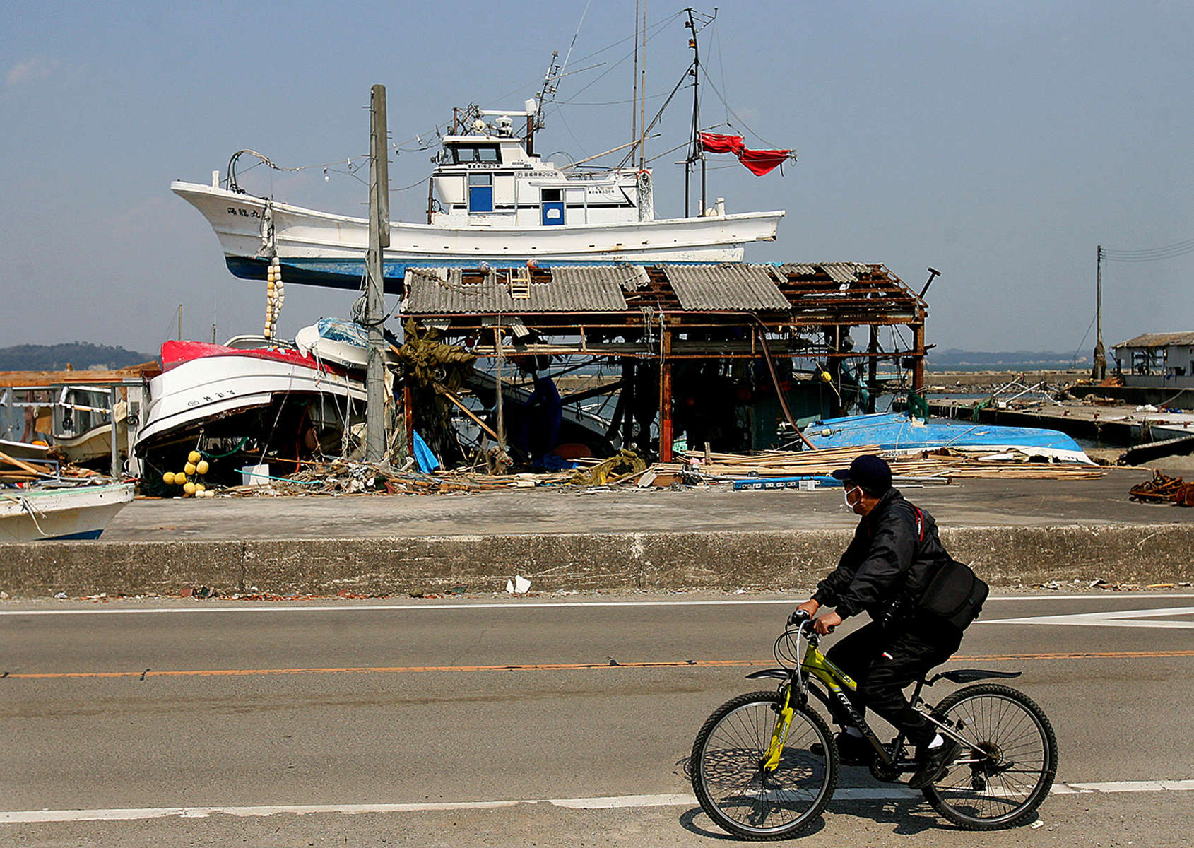 A man rides his bicycle past a fishing boat that landed on top of a building after a tsunami hit Shichigahama, a fishing town of northern Sendai, Japan. (The Press-Enterprise/ Mark Zaleski)