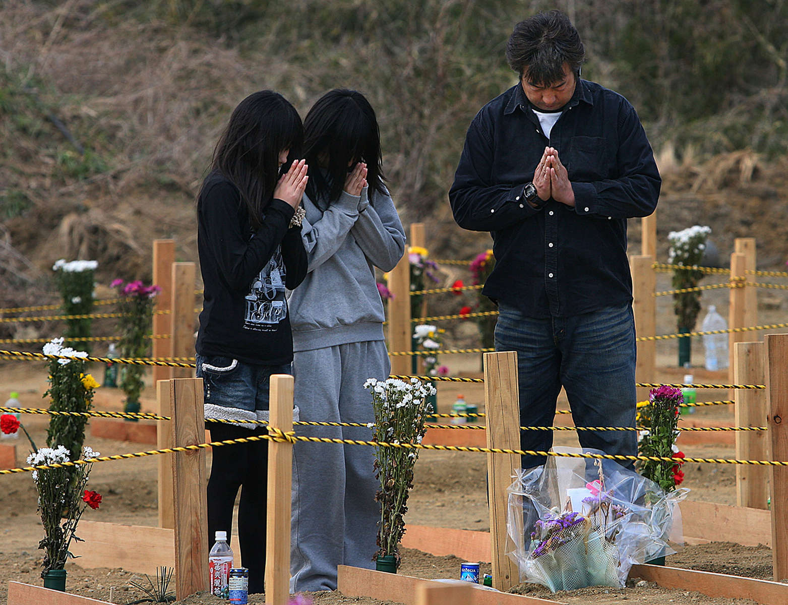 A man and his two daughters pray over a grave at a temporary burial site near a recycling centerin Higashimatsushima, a ward of Sendai, Japan. (The Press-Enterprise/ Mark Zaleski)