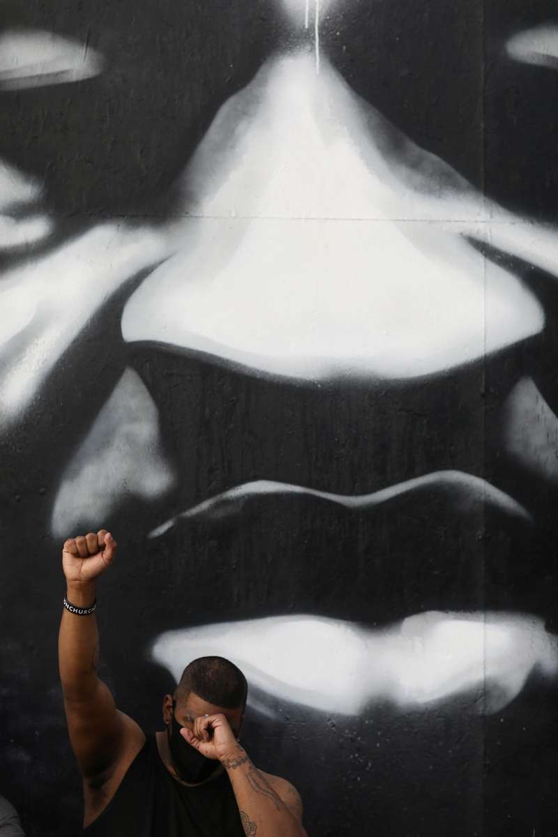 A young man raises his fist as he sits in front of a mural of George Floyd at a memorial site for Floyd outside of Cup Foods June 2, 2020. The memorial is located at the site where Floyd was pinned to the ground by Minneapolis police for over eight minutes even as he plead that he couldn't breathe until he became unresponsive and was later pronounced dead in Minneapolis. The protester, who preferred not to be named, said he was one of the witnesses on the street who recorded the death of Floyd on his phone.