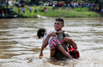 A man clutches on to a child, both of them members of a caravan traveling to the U.S., as he struggles to cross the Suchiate river from Guatemala to Mexico in Ciudad Hidalgo. 