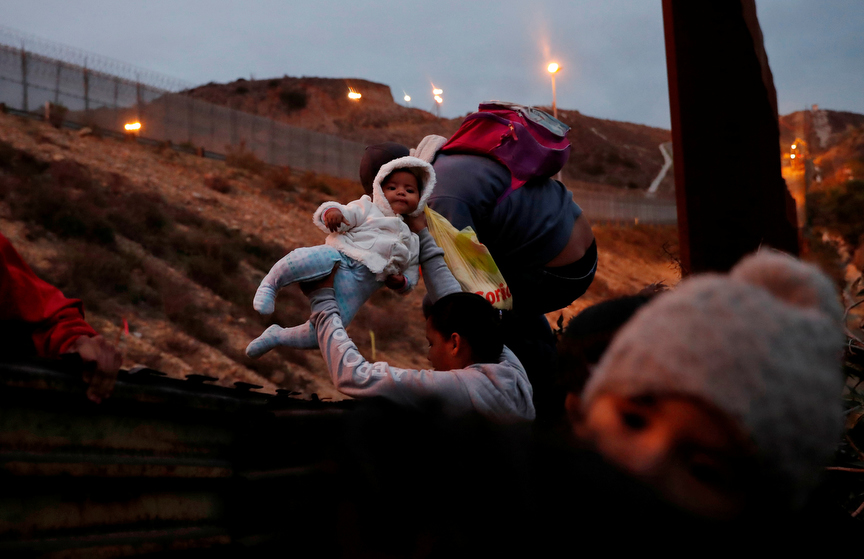 Honduran migrants, part of a caravan of migrants from Central America traveling with the intention of reaching the U.S. jump over a border fence into the U.S. from Tijuana, Mexico December 14, 2018. REUTERS/Leah Millis