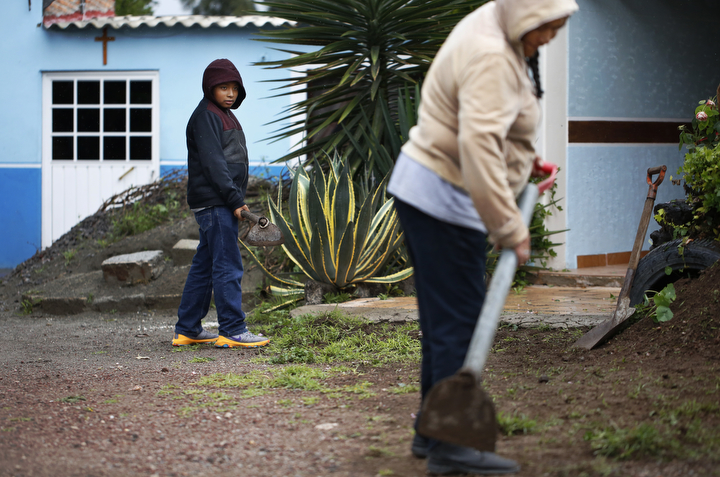 Jesus Sanchez, 12, watches his grandmother Juana Alamilla Olguín, 69, for technique as he helps clear weeds in front of her house as a light rain falls Sept. 30, 2017 in Santa Monica, Hidalgo, Mexico.