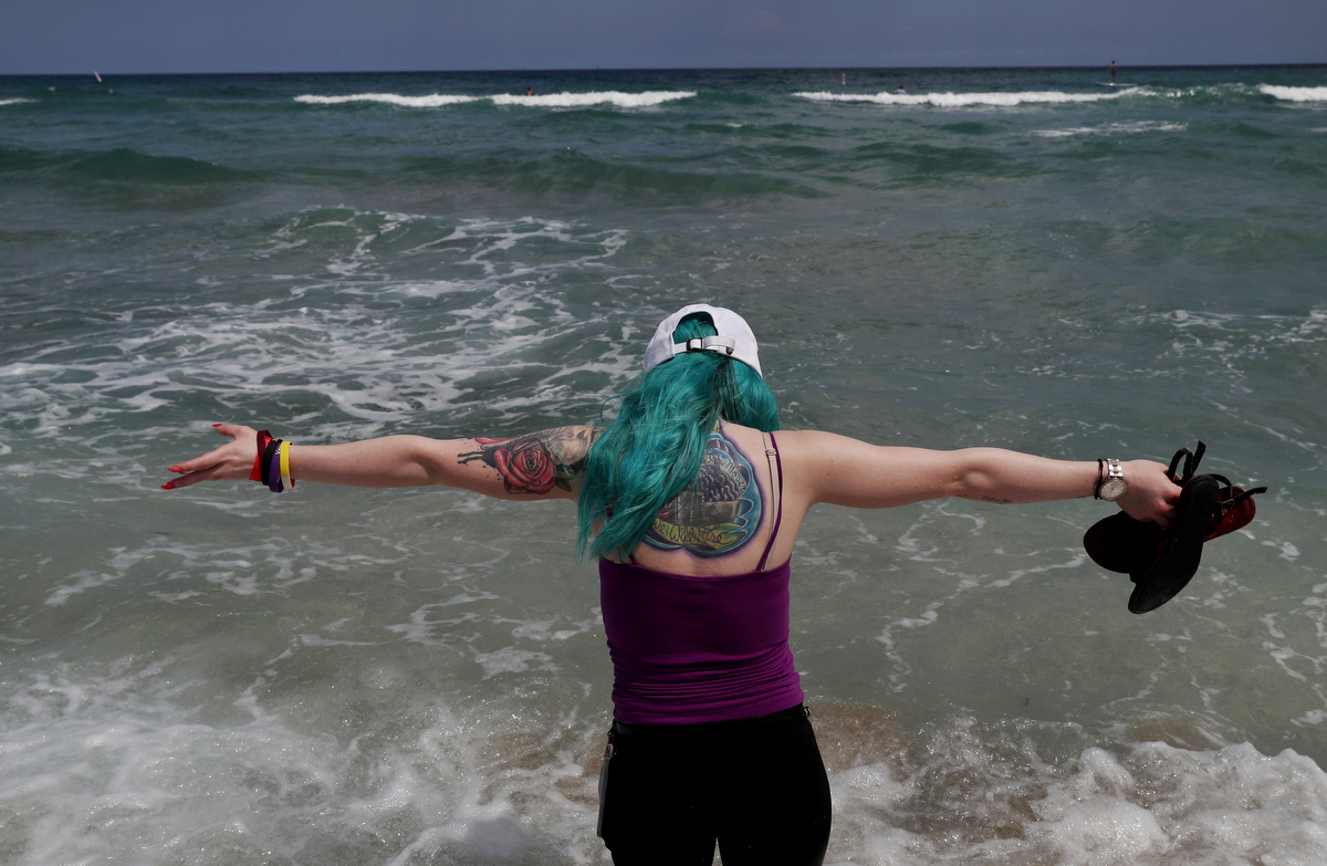 Kaylan Bailey, 20, a survivor of the Aurora Theater shooting, takes in the ocean as she visits the beach with Heather Martin of Columbine and Sherrie Lawson of Washington Navy Yard April 2, 2019 near Ft. Lauderdale, Florida, US. On her back, a tattoo memorializing the event can be seen. The Rebels Project members were invited to Florida to participate in a Parkland MSD Community Peer Support Event.