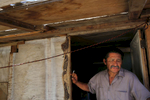 While trying to shelter from triple digit heat, Martín Hernandez Mena, 50, smokes a cigarette as he stands in the doorway of the home he built in the shantytown. Mena has lived for a year and a half in the canal bed. He moved after he could no longer afford rent in town because work was becoming more and more scarce.