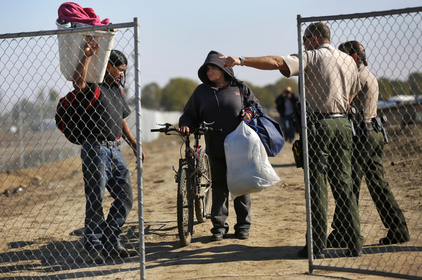Maricela Montejano, 49, center, and Gerardo “Gerry{quote} Anzorena, both residents of the shantytown, clutch their belongings as they are directed by Fresno County Sheriff's officers out of a temporary fence line surrounding the encampment during the eviction.