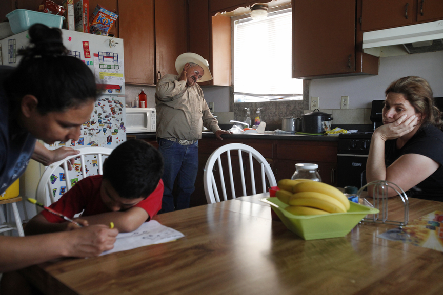 Both unemployed, Jose Pineda Rivas, 61, center, stands in the kitchen with his wife, Maria Callejas, 43, right, as Ruth Fuentes, 32, left, helps her son Jose, 6, with his homework at Fuentes' home April 10, 2014 in Mendota, Calif. Rivas and his wife have been living with the Fuentes' family for four years. Rivas came to the United States in 1988 and was joined by his wife 3 years ago. They left five children behind in El Salvador, who they send money to every month. Both Rivas and his wife work in the fields for their income. Right now neither of them have been able to find steady work and the stress is taking its toll. Rivas has been having trouble sleeping and eating due to a constantly upset stomach and a toothache he cannot afford to repair. 