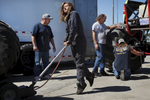 Rosalee Ramer, 16, throws all of her weight onto the handle of a floor jack, using it to raise up her father's monster truck so she can put monster wheels on it as Guillermo Serrano, left, Kelvin Ramer (her father), third from left, and Dave Wever work on her truck in preparation for their evening performance.