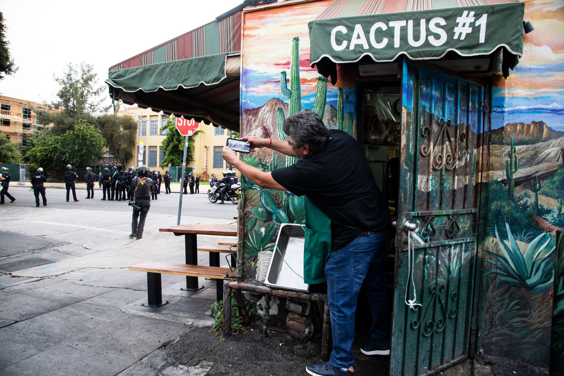 A man get out of his store briefly to take pictures of police arriving to enforce curfew over protesters  during a march over the death of George Floyd, an unarmed black man, who died after a police officer kneeled on his neck for several minutes, in the Hollywood neighborhood on June 1, 2020, in Los Angeles, California.