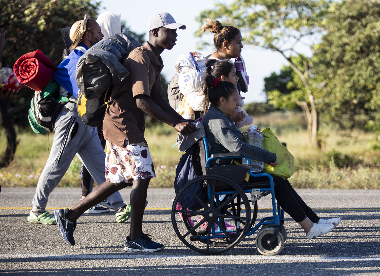 A migrant pushes a wheelchair with the mother of a family he befriend,  as they walk along a road in a caravan heading to the northern border,  in Chahuites, Mexico November 8, 2021. 