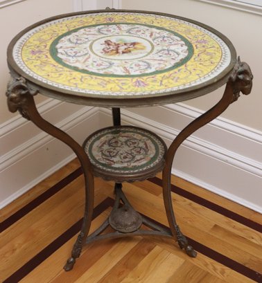 Elegant French-style porcelain and bronze mounted gueridon side table featuring ram’s head accents. The crackled porcelain is adorned with scrolled vines and tendrils, showcasing a trio of cherubs atop sheaves of golden wheat in the center.25” dia x 28” hOur Price  $2,100