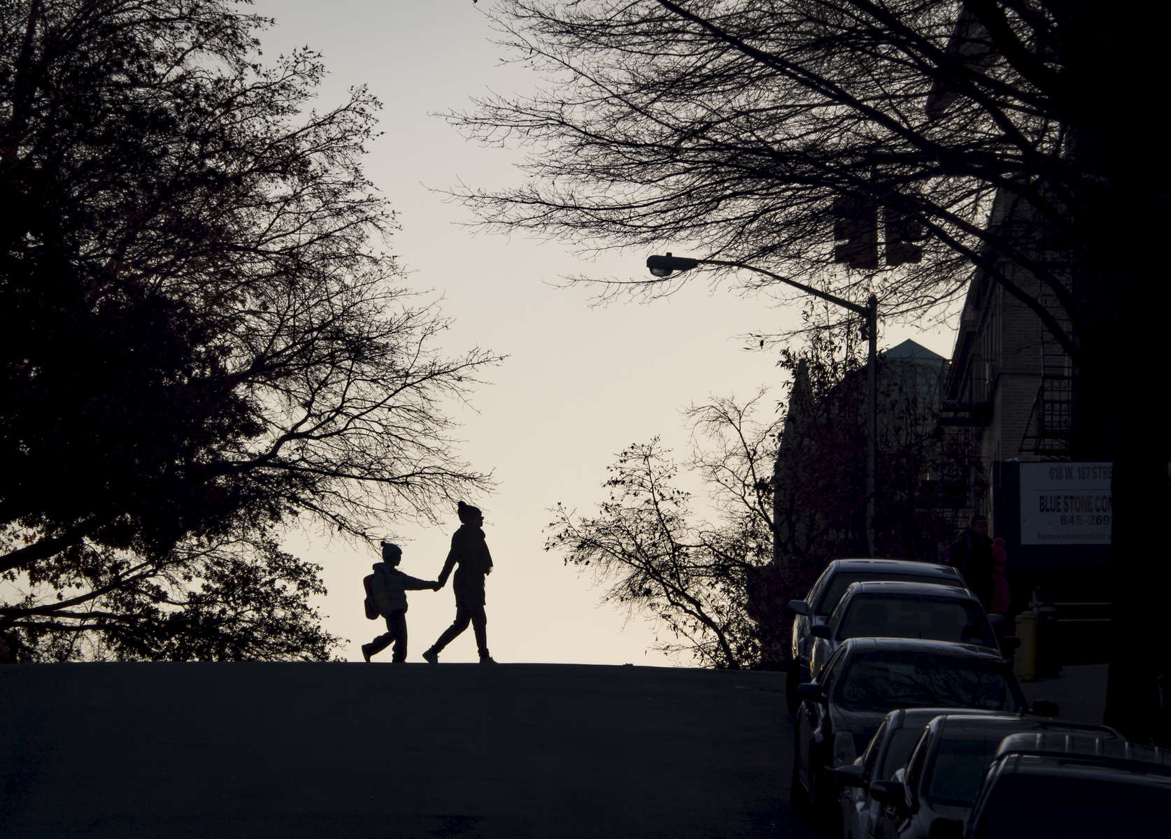 A woman and a child are both silhouetted as they cross the street early in the morning at the corner of 187th Street and Wadsworth Avenue in Washington Heights in Manhattan on Friday, December 9, 2016. 