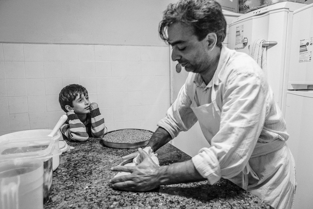 Nour watches as his father Ayman prepares Syrian pasteries in their new home on the outskirts of São Paulo. Nour recalls as this entire family spent 17 days at sea in summer of 2015, and how his father, make risotto with salt water. Bound for Italy, their boat was intercepted by the Egyptian authorities, who arrested all 227 people onboard. The Syrian embassy refused to repatriate the family, so they applied for asylum to Brazil. Ayman, a resourceful 41 year old father of 2, say, {quote} In Brazil we are neither Shiete, or Sunni, Muslim or Christian. Veil or not. We are human. And so, I am happy.{quote}