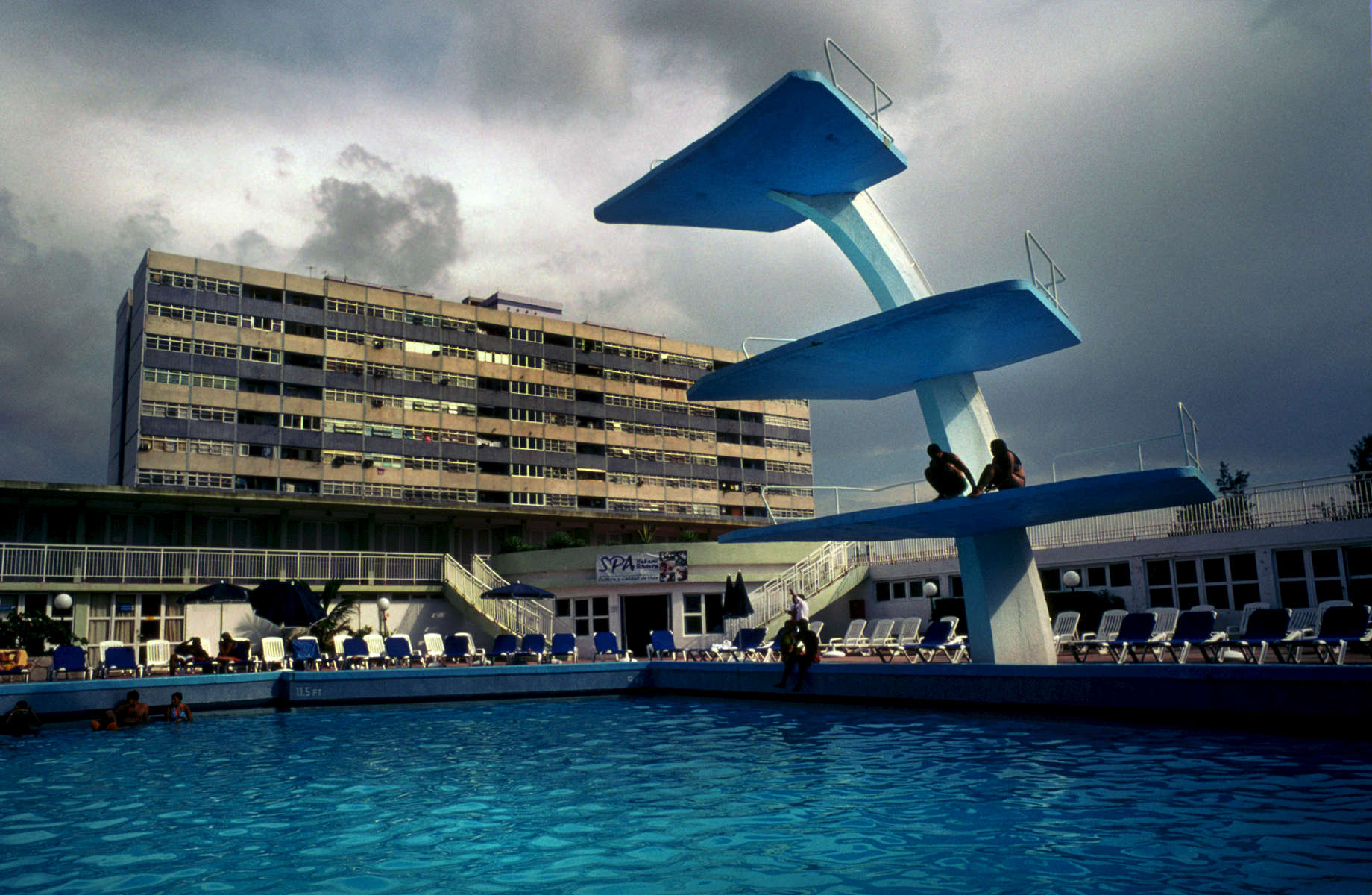 Many tourists bask in the summer sun, blistering their skin at one of the many hotel pools and resorts. For many years, Cubans were not allowed access to the hotels or resorts and their amenities. Today, some hotels will allow Cubans, for a small fee, to enter their premises allowing access to the pools, restaurants, and bars, yet it can still be cost prohibitive for many local people.  Hotel Habana Riviera is a popular, late 1950's, art deco-styled hotel, which was being built in the midst of the revolutionary upheavel. It was envisioned as the {quote}The Riviera of the Caribbean,{quote} as it was considered the epitome of resort-construction, with the first of its kind to have ariconditioned rooms. A concrete, Russian housing development strategically juxtaposes the background of the art-deco, architecture of the Riviera, reminding its guests of the communist / anti-capitlist regime. 