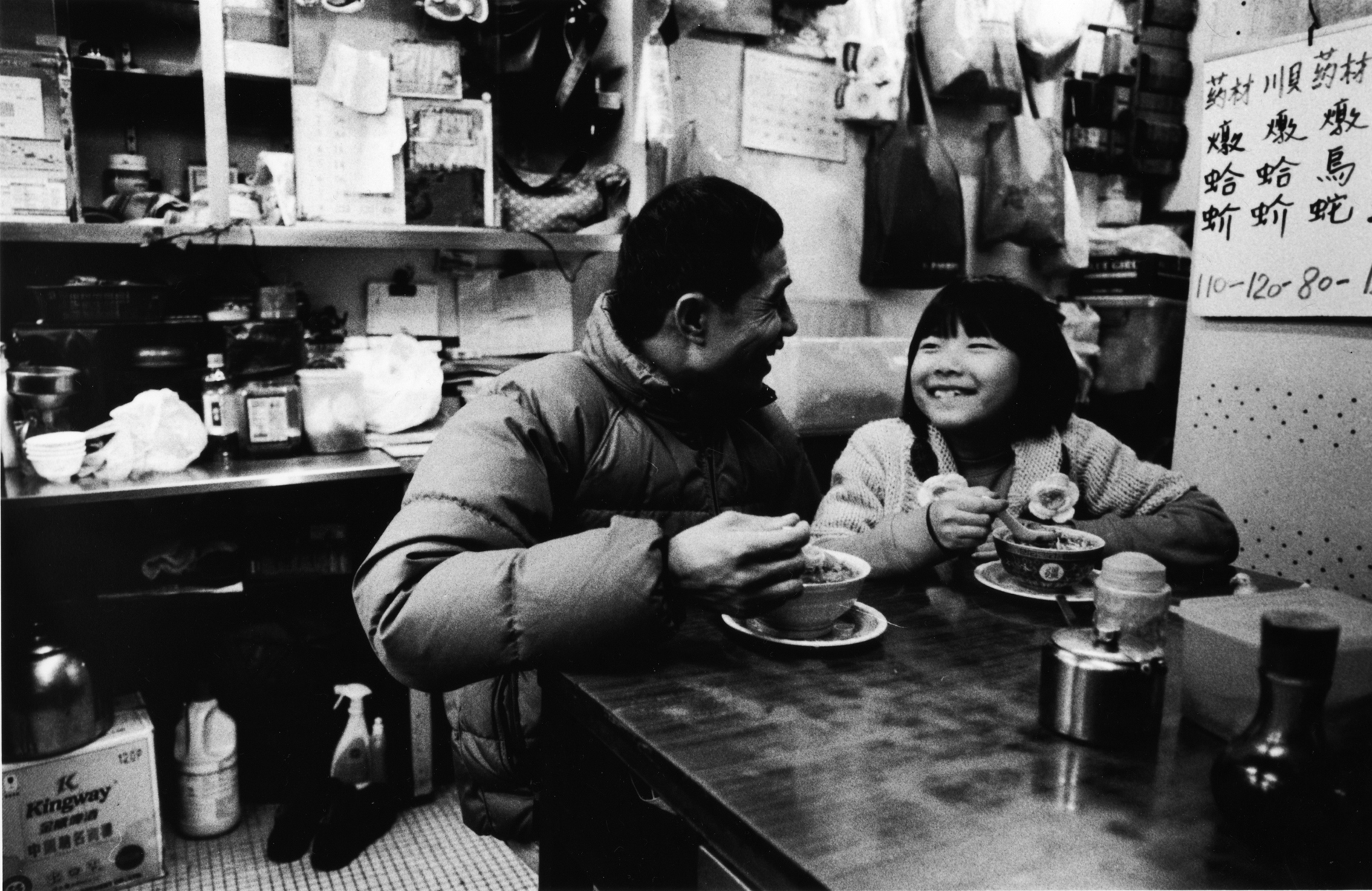 A father enjoys a bowl of noodles with his daughter. Kowloon Peninsula, Hong Kong