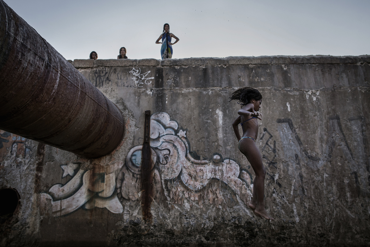 A group of teenegers jump from a water pipe in a sewage that separates the beaches of Ipanema and Leblon, in Rio de Janeiro, Brazil, February 03, 2012.While many believe that UPPs have helped quell violence by opening the doors of the favelas to public services such as legal electricity supply, garbage collection, education, public works and social assistance program, others see the pacification program as a temporary cover-up to security problems in Rio de Janeiro. 