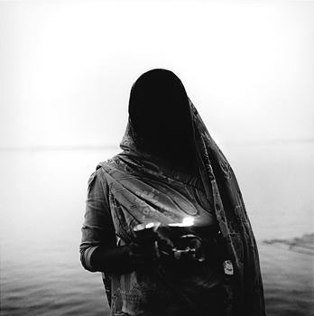 A Hindu woman makes and offering and prays before casting the candles she holds into the Ganges River. Varanasi, India 1997