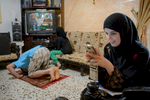 Sara Abed El Hade (16) checks the messages on her smartphone while her father Ahmed prays and her younger sister Amina watches television. Sara wants to become a graphic designer.