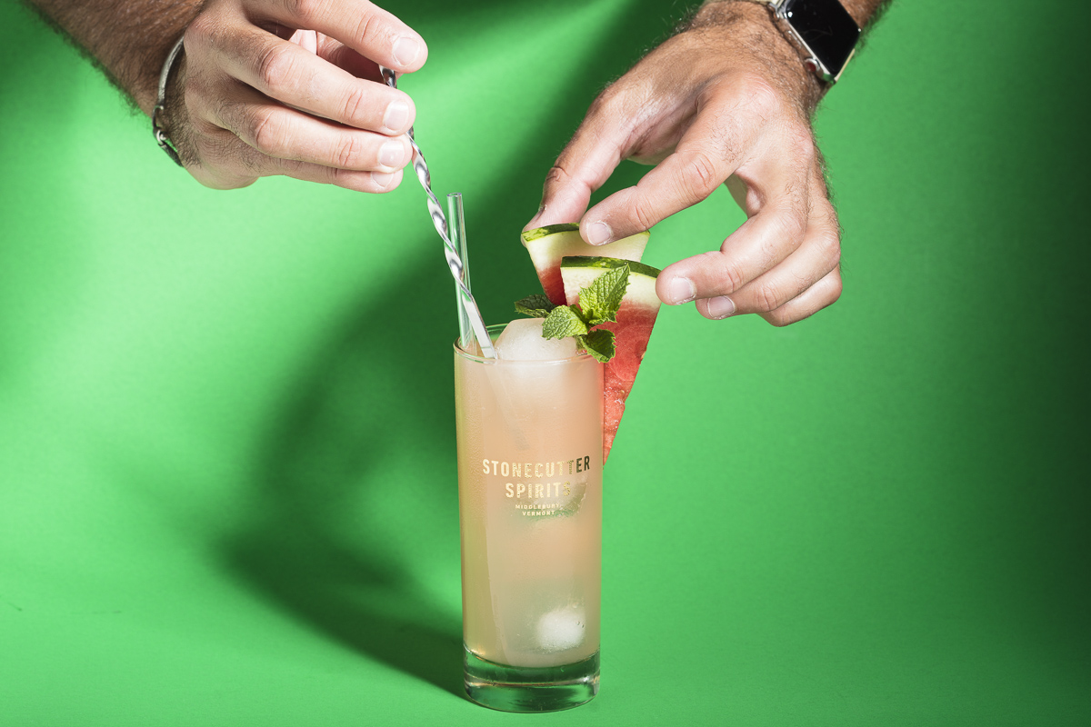Hands styling a Stonecutter Spirits cocktail with watermelon on a green background. By commercial photographers at JAM Creative.
