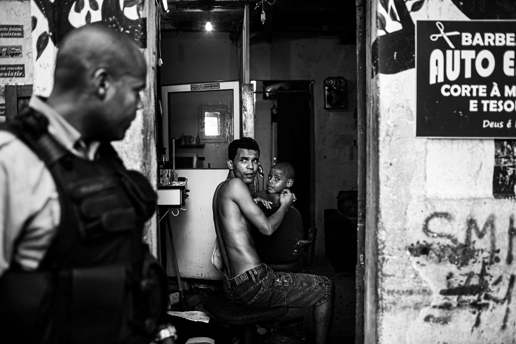 El soldado de la UPP. Franca, camina frente a una barbería mientras su dueño le corta el pelo a un cliente, en la favela de Sao Carlos, en Río de Janeiro, Brasil, el 15 de marzo de 2012.