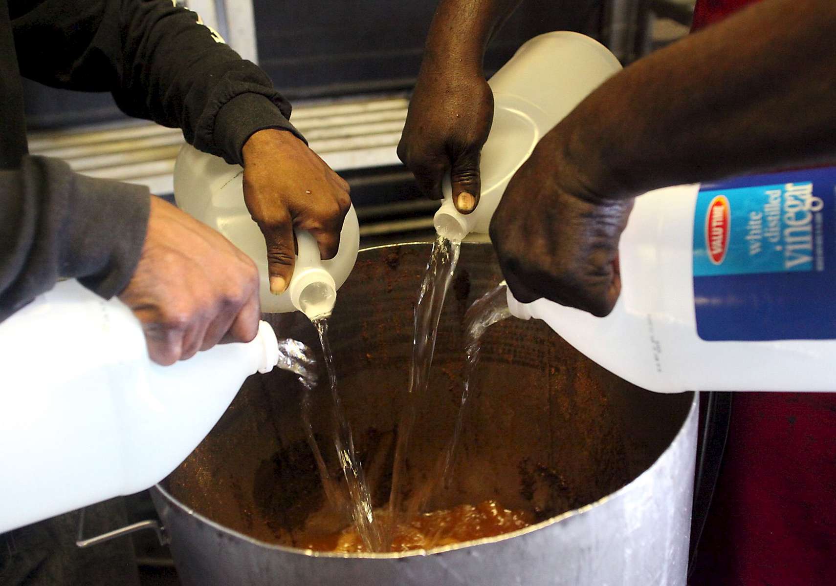 Pit workers Larry Mitchell (left) and Willie Johnson pour vinegar into a large pot at Scott's BBQ in Hemingway, South Carolina, June 21, 2012. The Southern Foodways Alliance and the University of Mississippi’s Center for the Study of Southern Culture made a stop at Scott's BBQ in Hemingway, S.C. to complete the month-long trip to gather and preserve the stories behind South Carolina’s barbecue culture during their ongoing documentary project, The Southern BBQ Trail. According to food historian Rien Fertel and photographer Denny Culbert, who are conducting the study, there are only ten or 15 BBQ pits in the whole South that use the old-timey methods of fire coal pit cooked BBQ they use at Scott's.  REUTERS/Randall Hill  (UNITED STATES)